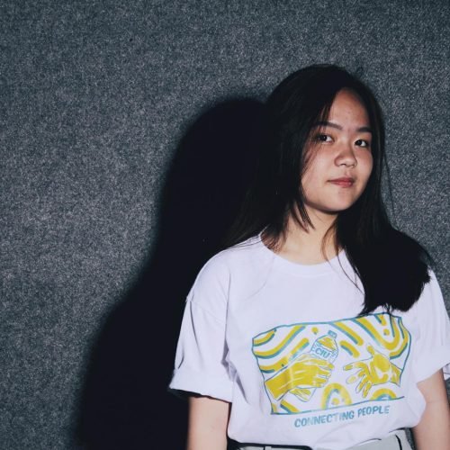 Young woman posing against a plain backdrop wearing a trendy t-shirt, showcasing casual style and confidence.
